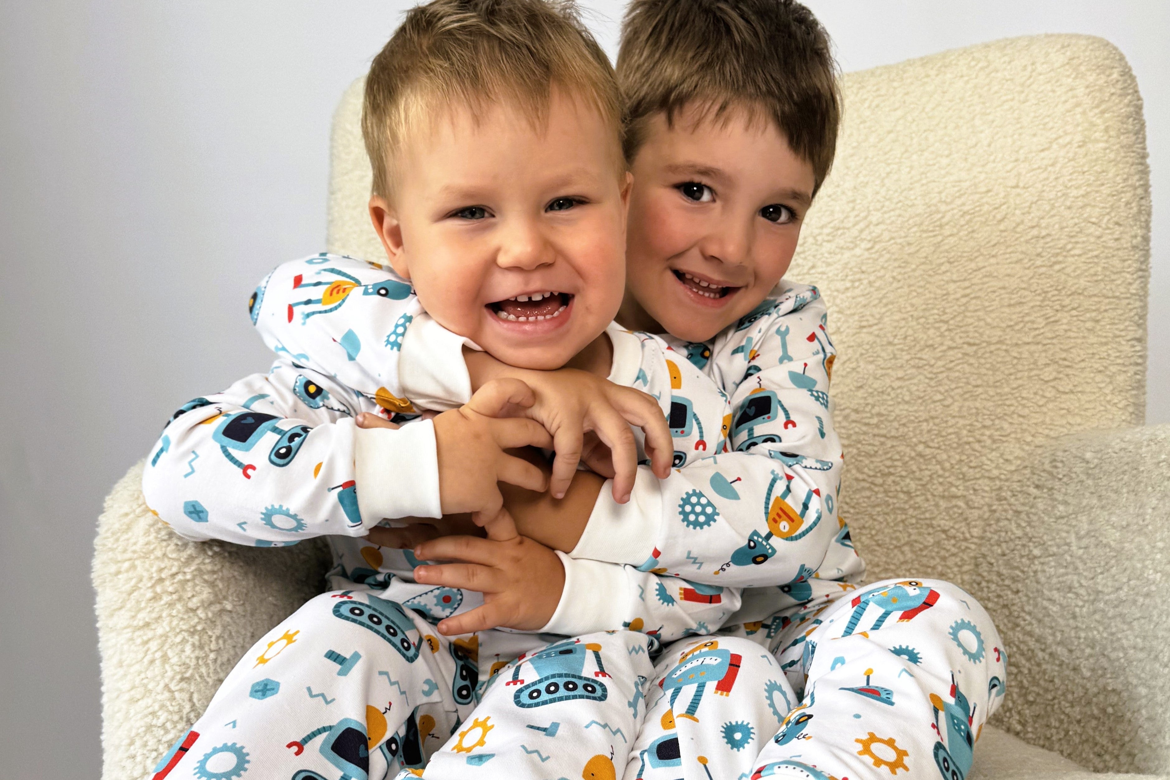 Two children in pajamas with vehicle patterns sitting on a beige chair.